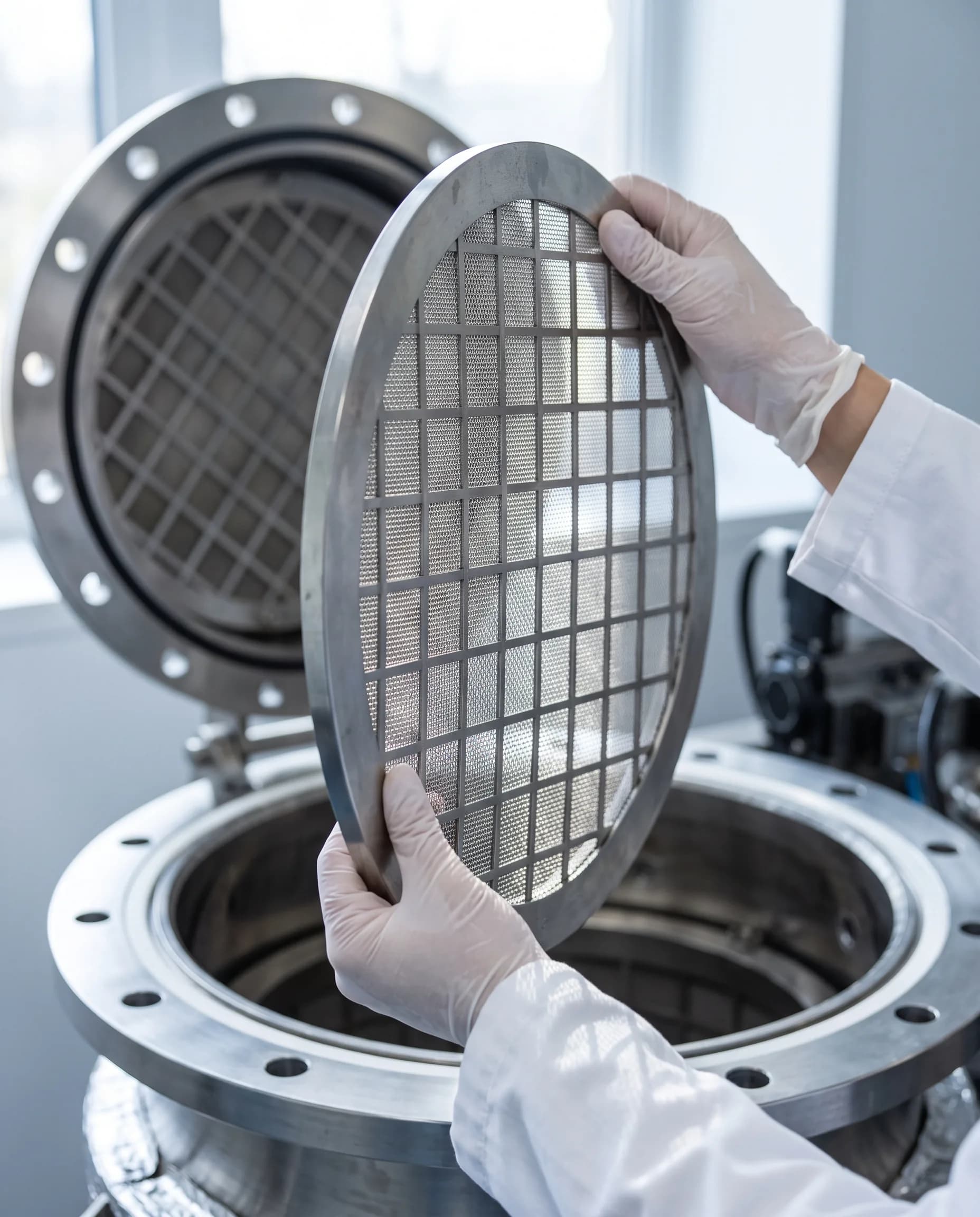 Gloved hands holding a stainless mesh filter plate over an open vessel